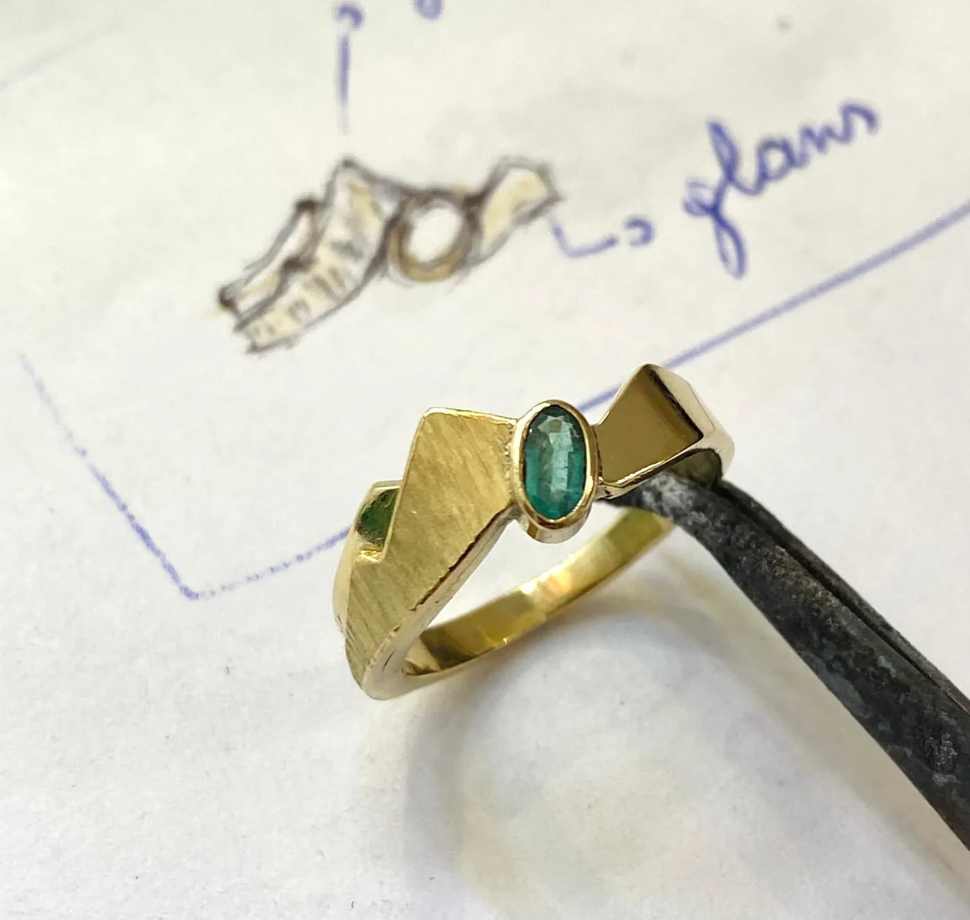 Gold ring with a green stone, on its design sketch