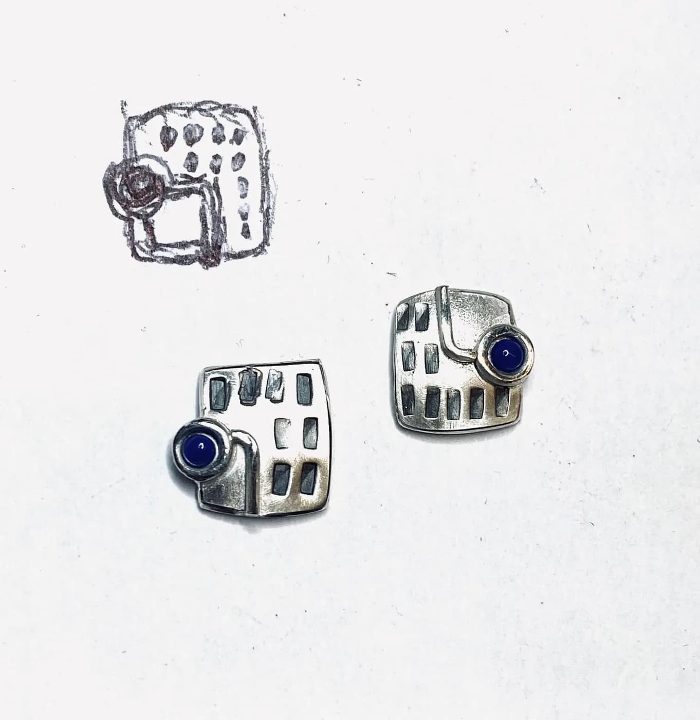 Silver stud earrings next to their design sketch